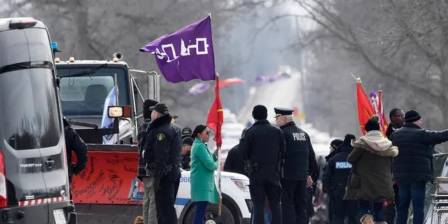 A woman speaks with Ontario Provincial Police officers as she removes flags from a rail blockade in Tyendinaga Mohawk Territory, near Belleville, Ont., on Monday Feb. 24, 2020, during a protest in solidarity with Wet'suwet'en Nation hereditary chiefs attempting to halt construction of a natural gas pipeline on their traditional territories. (Adrian Wyld/The Canadian Press via AP)