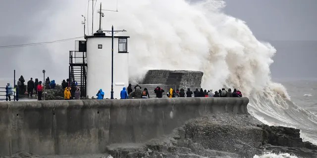 People watch waves and rough seas pound against the harbor wall at Porthcawl in Wales, as Storm Dennis sweeps across the country, Saturday Feb. 15, 2020.