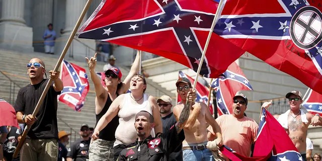 Members of the Ku Klux Klan yell as they fly Confederate flags during a rally at the statehouse in Columbia, South Carolina July 18, 2015. A Ku Klux Klan chapter and an African-American group planned overlapping demonstrations on Saturday outside the South Carolina State House, where state officials removed the Confederate battle flag last week. REUTERS/Chris Keane? TPX IMAGES OF THE DAY - GF10000163673