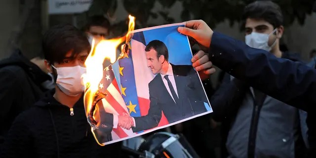 Iranian protesters burn a picture of French President Emmanuel Macron and President Donald Trump during a protest against Macron and the publishing of caricatures of the Prophet Muhammad they deem blasphemous, in front of French Embassy in Tehran, Iran, Wednesday, Oct. 28, 2020. (AP Photo/Ebrahim Noroozi)