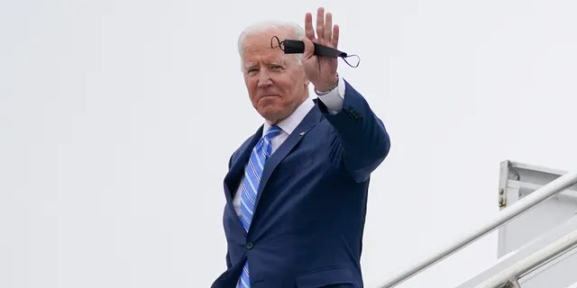 President Joe Biden holds his face mask and waves as he exits Air Force One at Capital Region International Airport, Tuesday, Oct. 5, 2021, in Lansing, Mich. 