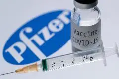 A syringe and a bottle reading "COVID-19 Vaccine" are featured next to the Pfizer company logo. (Photo credit: JOEL SAGET/AFP via Getty Images)